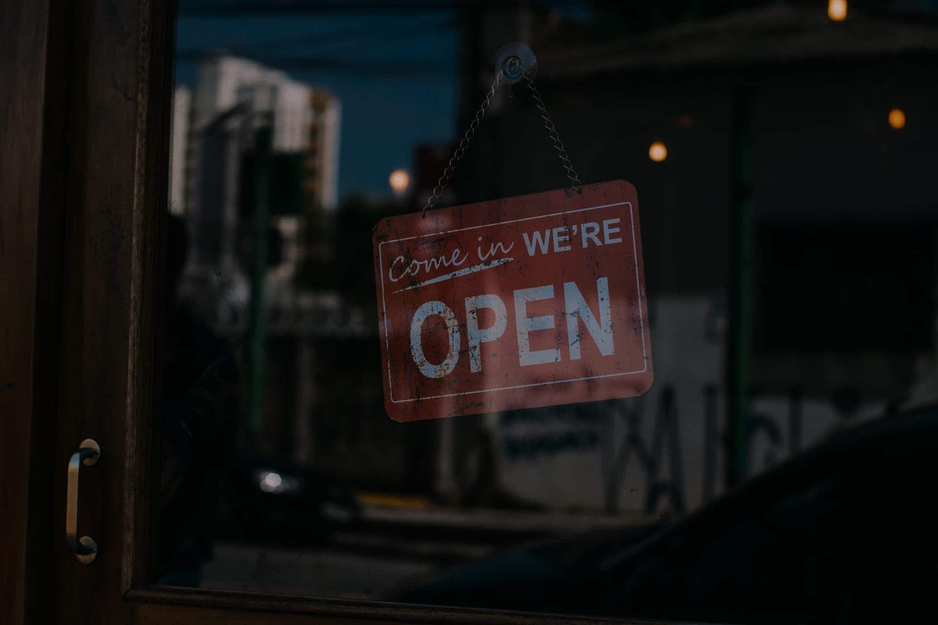 A sign hanging in a door reads Come In We're Open